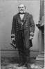 Henry Beauchamp Nones, full length portrait, standing, holding hat, facing slightly left - in uniform. Naval engineer