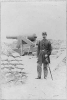 Union officer standing, full lgth., in front of sand-bagged cannon emplacement.
