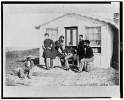 Five Civil War soldiers gathered on dirt porch outside home, African American youth seated near them