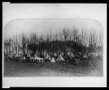 Union Army camp showing large tents errected among trees and soldiers posed by row of small tents